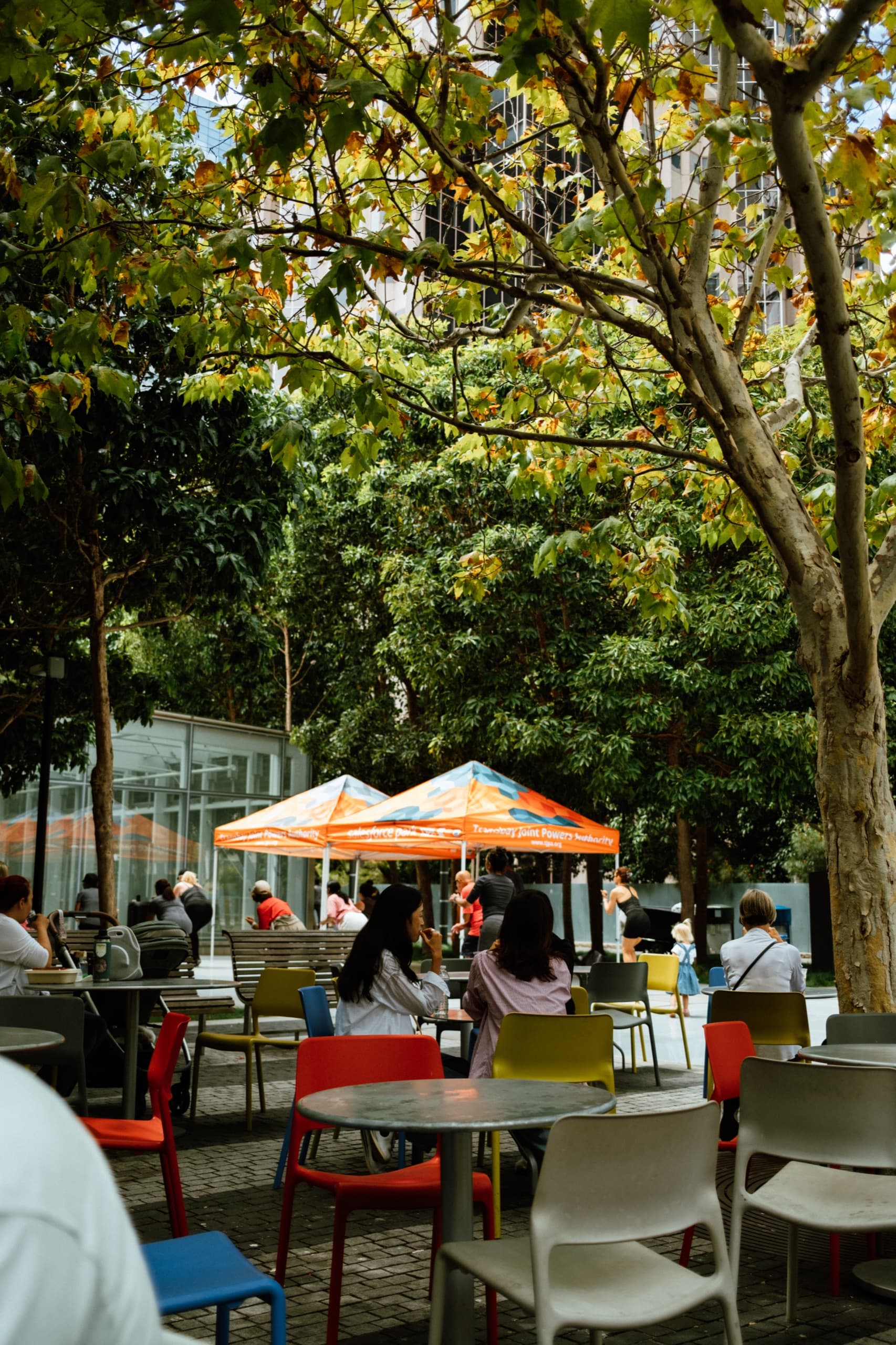 People at colorful tables under trees in Salesforce Park, orange tents behind them.