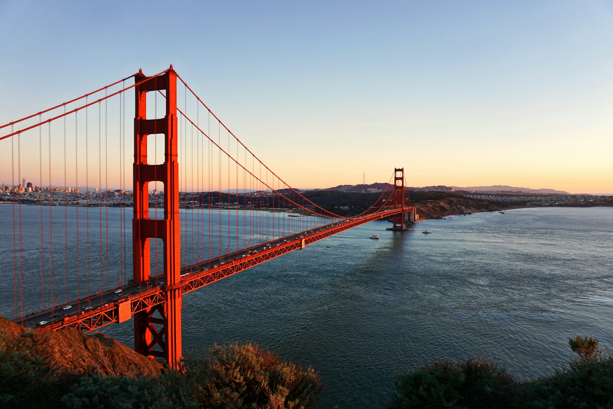 Golden Gate Bridge at dusk seen from the Marin Headlands, city lights beginning across the bay