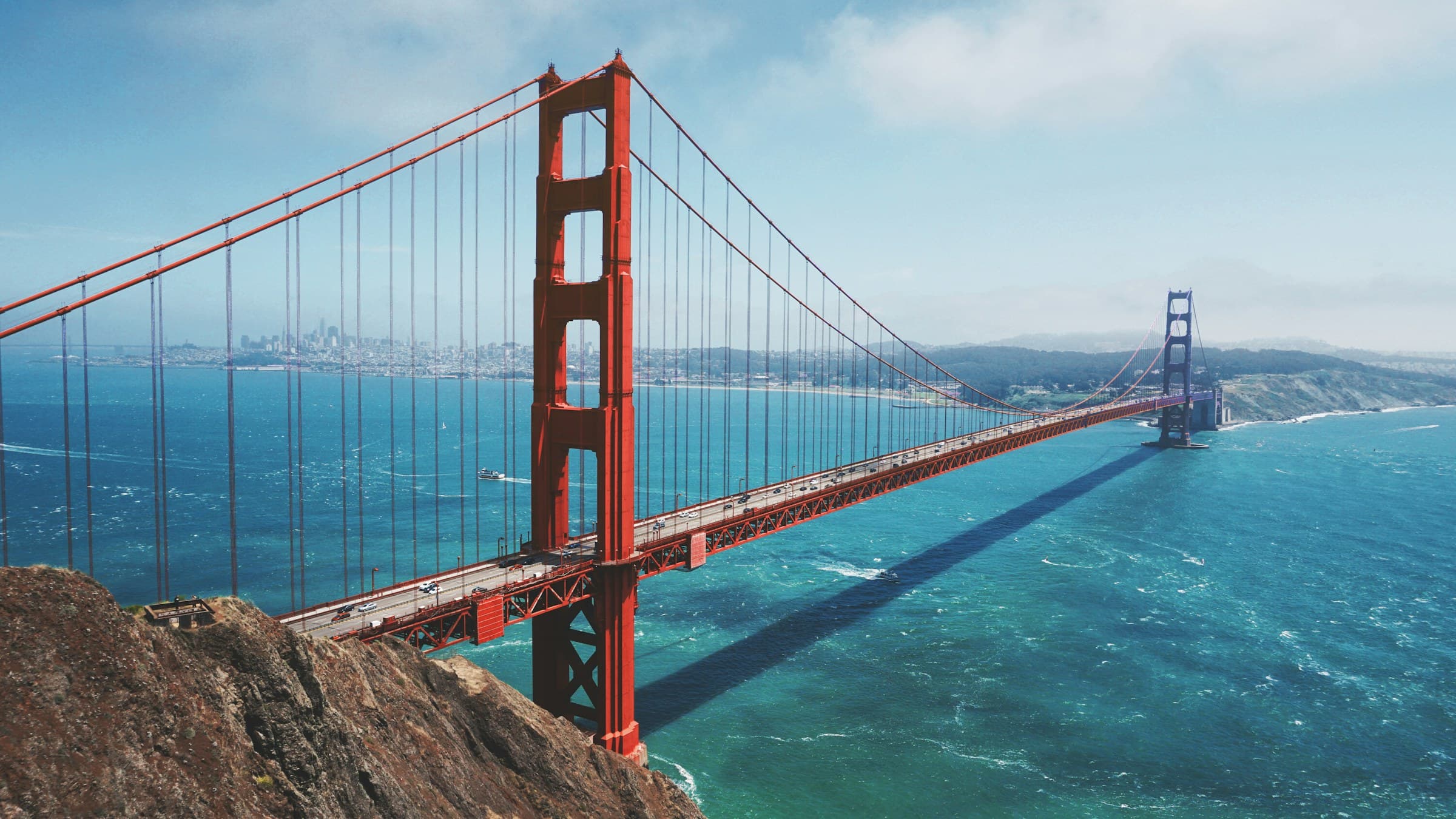 High-angle view of the Golden Gate Bridge, teal water and the city in haze