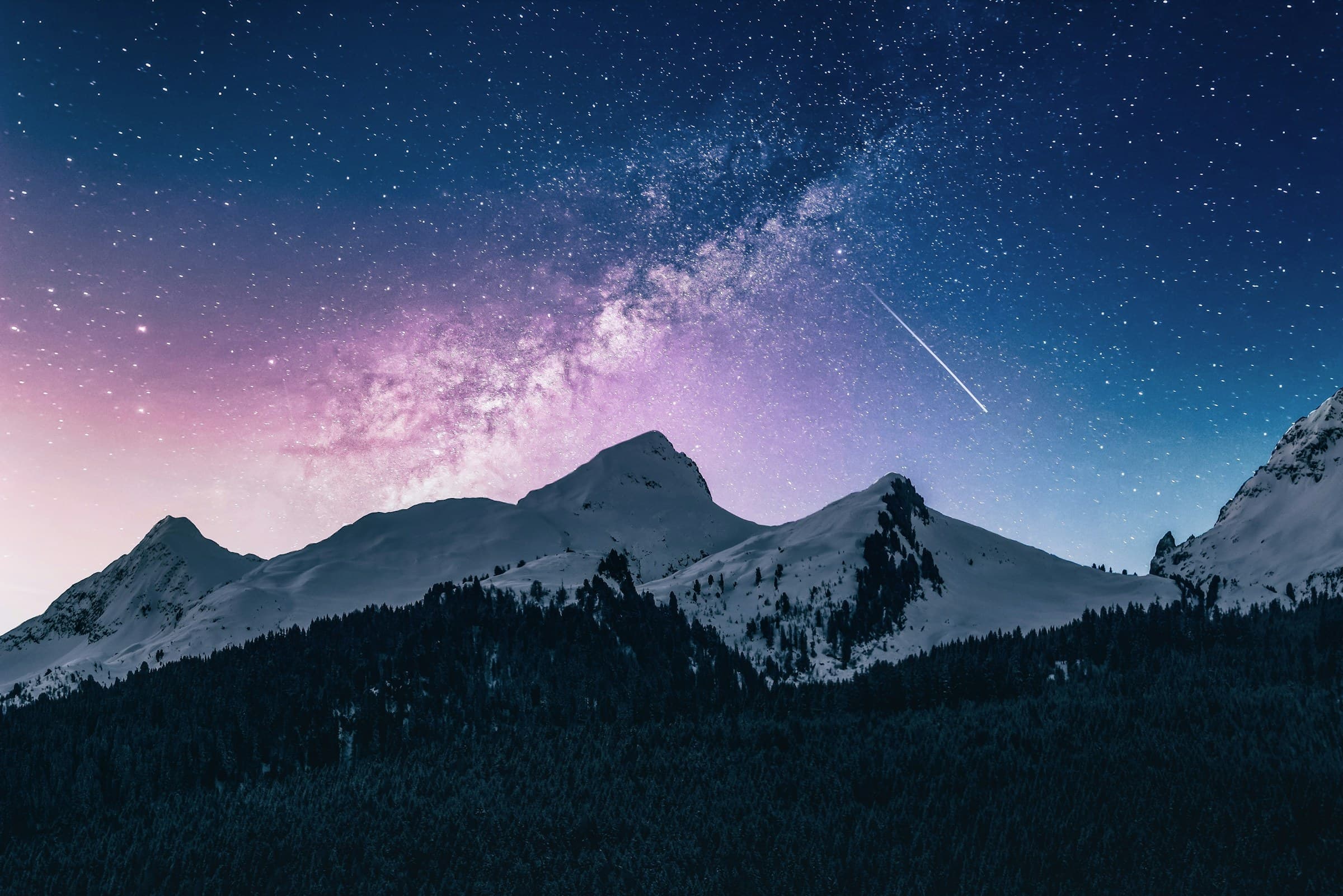 Starry night sky over a dark mountain ridge with snow